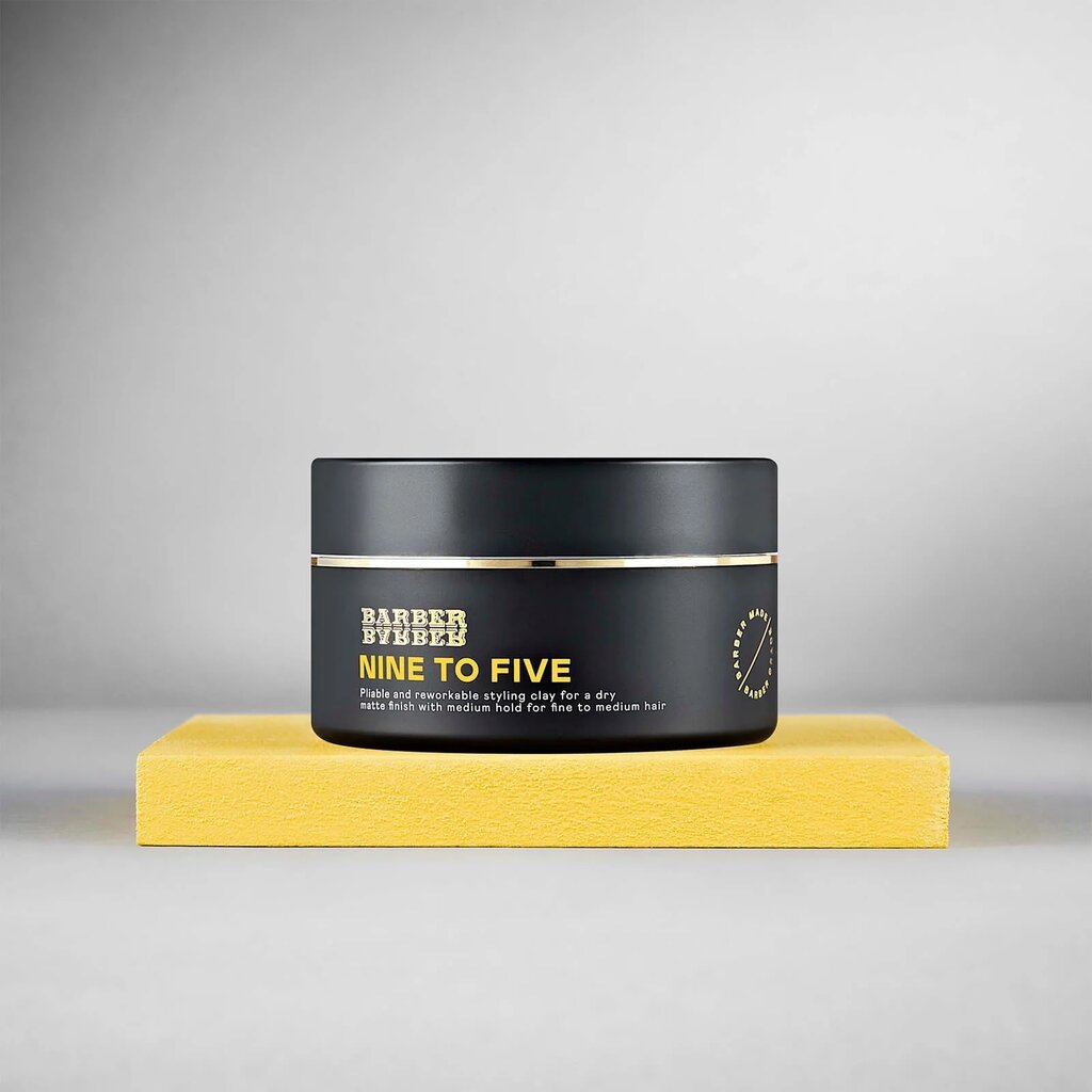 BARBER BARBER Nine To Five Medium Hold Styling Clay 100g, tarro negro sobre bloque amarillo, estudio gris