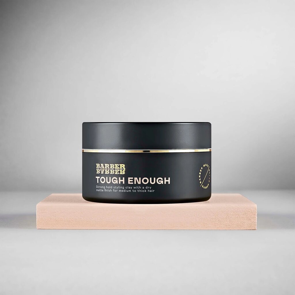 BARBER BARBER Tough Enough Strong Hold Styling Clay 100g, tarro negro sobre bloque beige, estudio gris