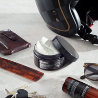 Bullfrog Strong Adhesion Matte Wax, open pot met witte wax in flatlay met helm, kam en zonnebril